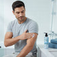 A man applying U&I Men in Blue hydrating body lotion to his arm in a bright, modern bathroom setting.