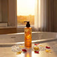 U&I Oud bath and shower gel in a 200ml amber bottle, displayed on a marble surface with rose petals by a window.