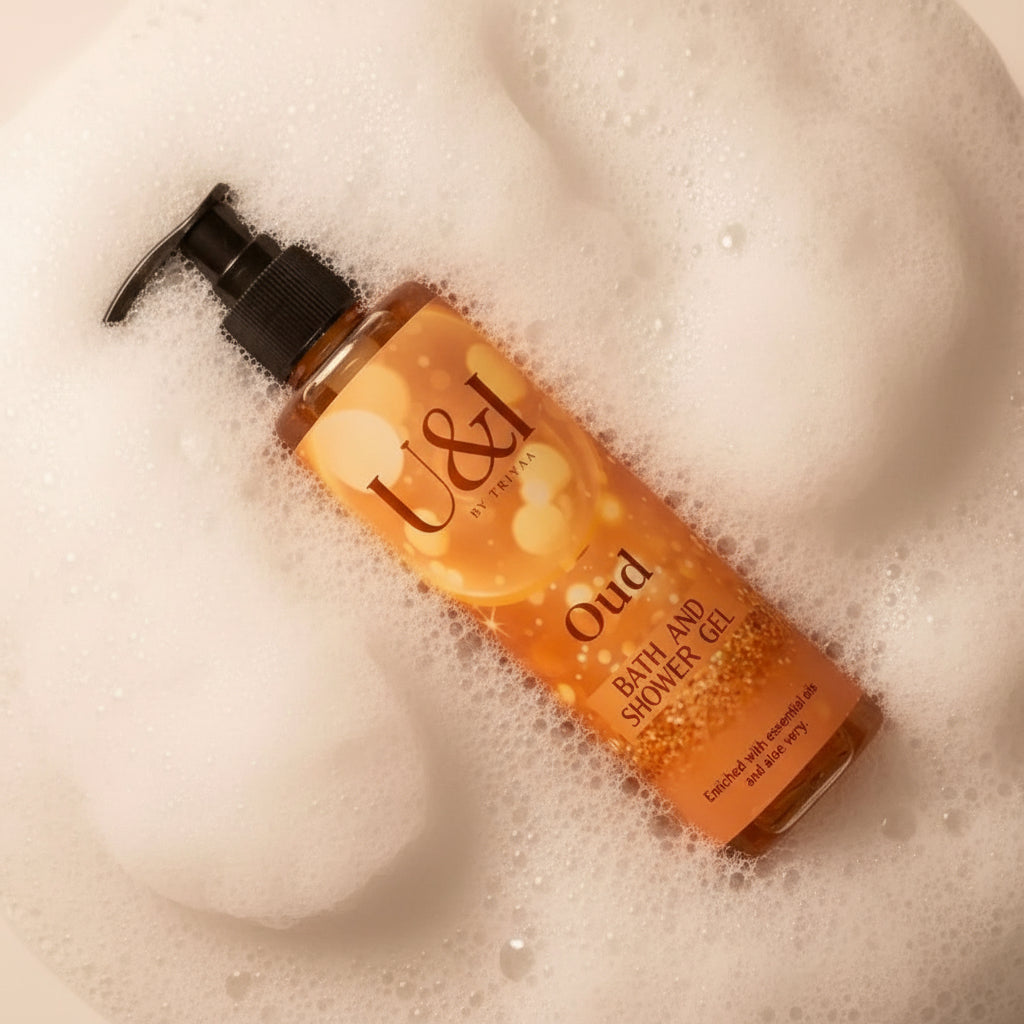 U&I Oud bath and shower gel in a clear pump bottle surrounded by white soap lather, featuring a warm golden label.