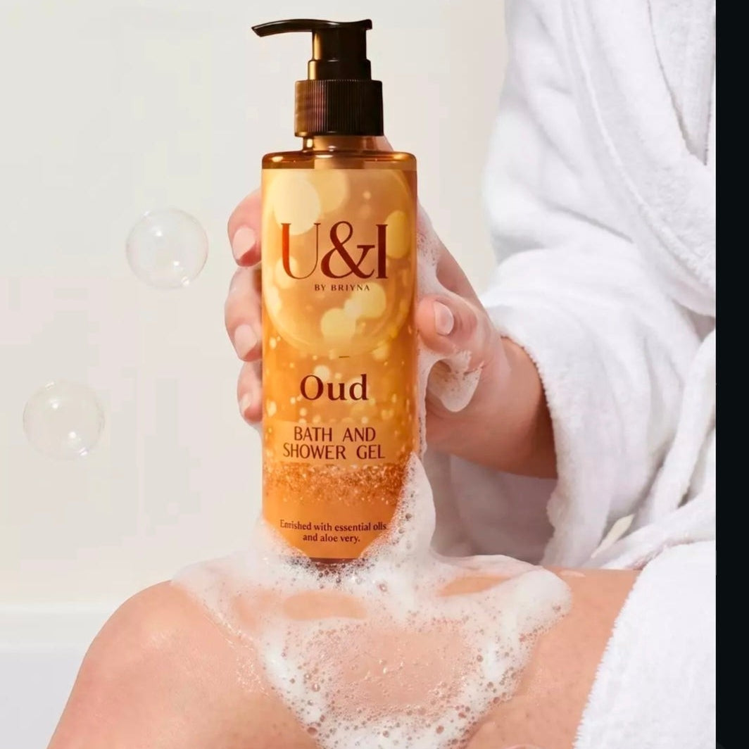 U&I Oud bath and shower gel in a 200ml amber pump bottle held by a person in a white robe with soap bubbles.