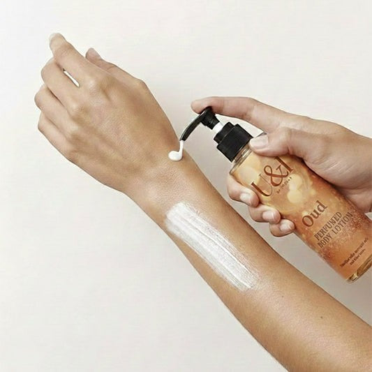 U&I Oud perfumed body lotion being applied to a person's arm, showing the creamy white texture and pump bottle.