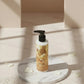U&I Oud perfumed body lotion in a 200ml pump bottle, displayed on a marble pedestal with scattered white petals.