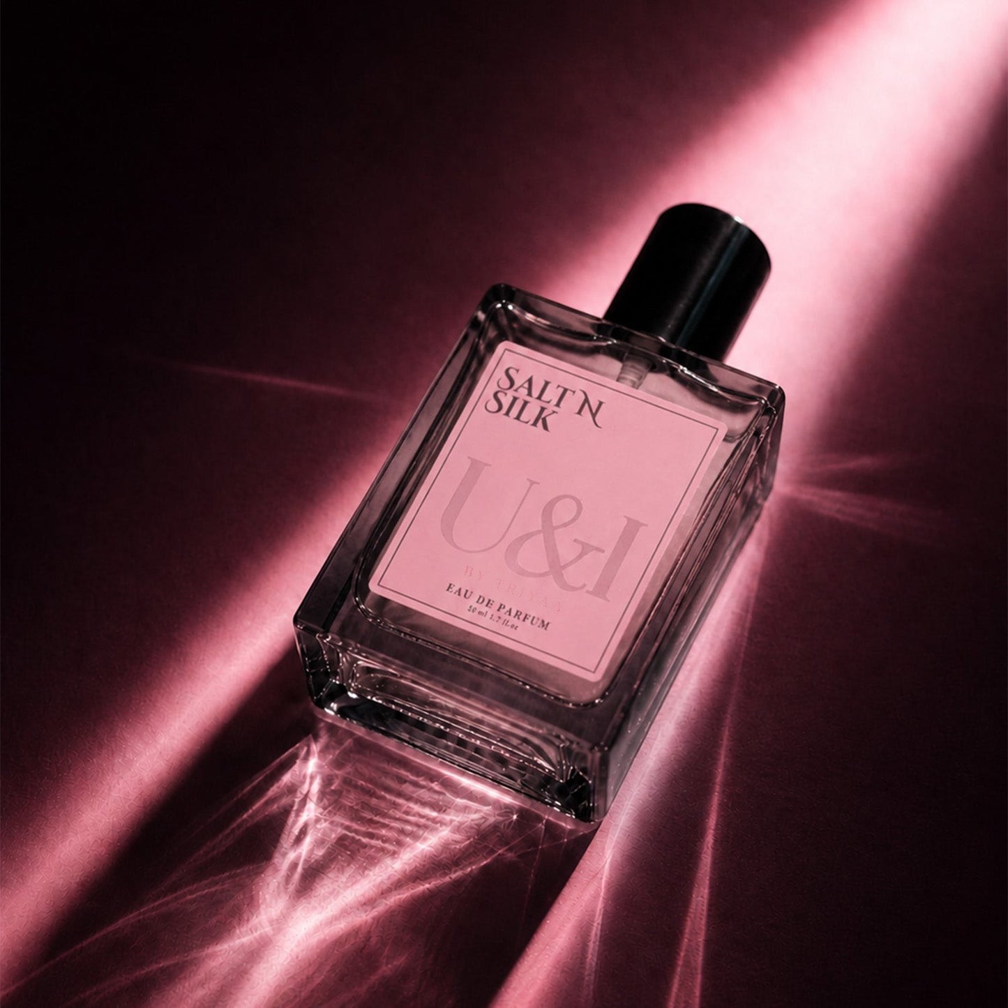 U&I Salt N Silk eau de parfum in a rectangular glass bottle with a black cap, illuminated by dramatic pink light.