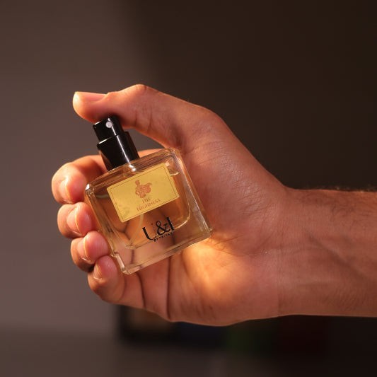 A hand holding a U&I His Highness perfume bottle with a gold label, featuring cedarwood and leather fragrance notes.
