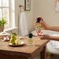 U&I Breeze of Eden perfume bottles on a wooden table with a fresh pear in a bright, serene bathroom setting.