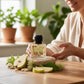 U&I Breeze Of Eden perfume bottle on a wooden table with fresh pear slices and green leaves, held by a smiling woman.