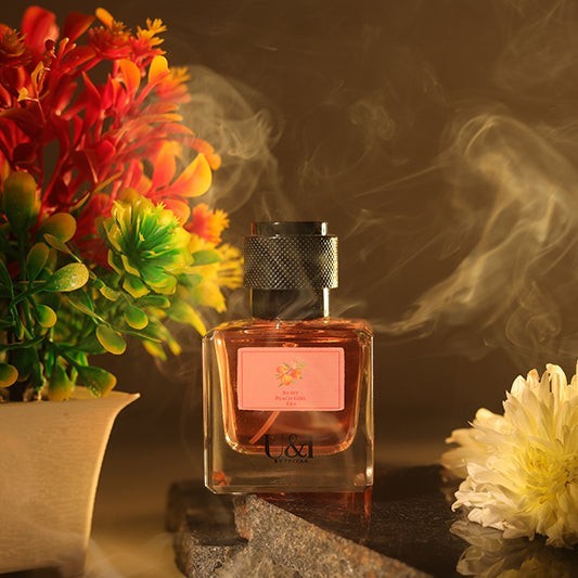 U&I In My Peach Girl Era perfume bottle with peach liquid, surrounded by flowers and soft smoke in a warm setting.