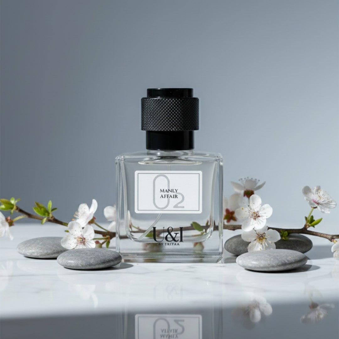U&I Manly Affair fragrance bottle on a white marble surface with grey stones and delicate white cherry blossom stems.