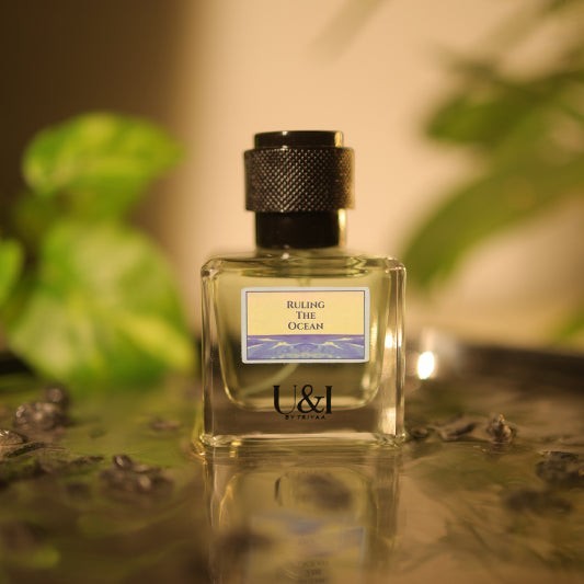 U&I Ruling the Ocean perfume bottle with a textured black cap, set in shallow water with soft green foliage background