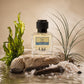 U&I Ruling the Ocean fragrance bottle on a stone with sea salt, driftwood, and seaweed against a sandy background.